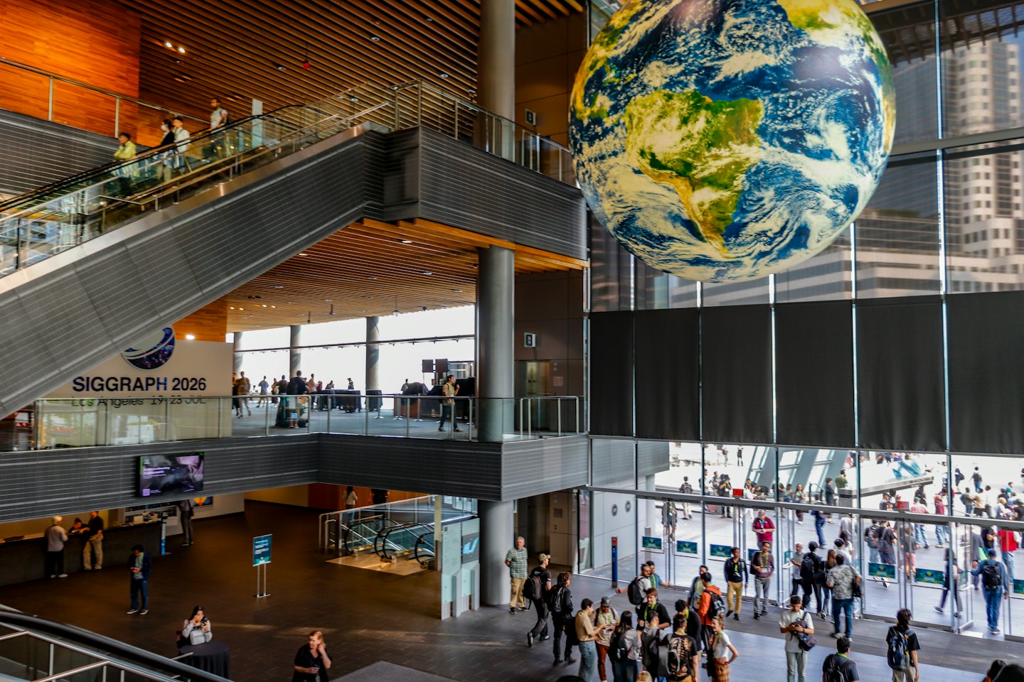 Gente caminando por un gran centro de convenciones bajo un globo terráqueo colgante.